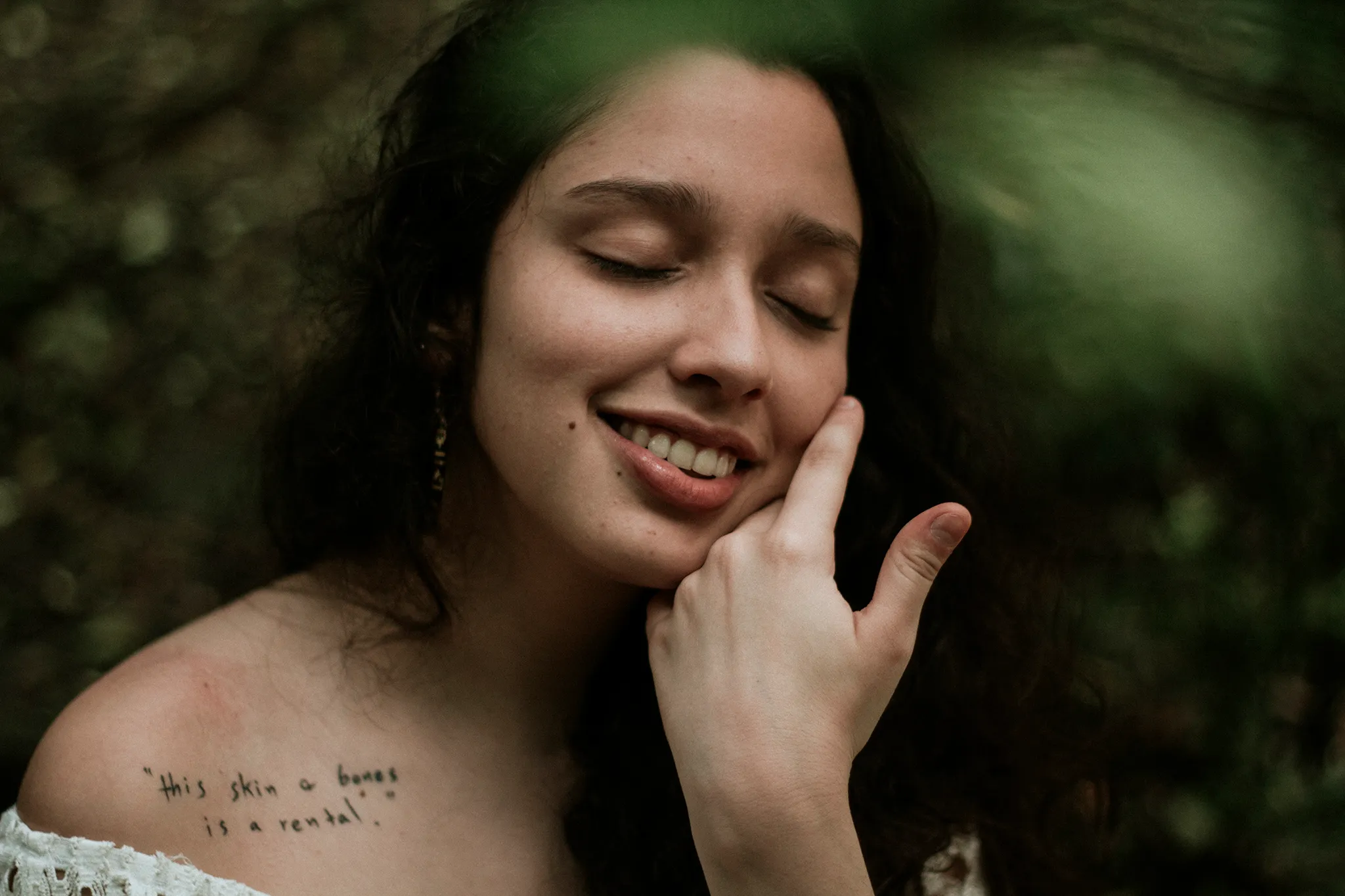 Dra. Andressa Paz sorrindo, mão no rosto, em meio à natureza